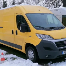 Ż&oacute;łty furgon dostawczy marki Fiat Ducato zaparkowany na śniegu, z pomarańczowo-białym pachołkiem drogowym w pobliżu przedniego koła.