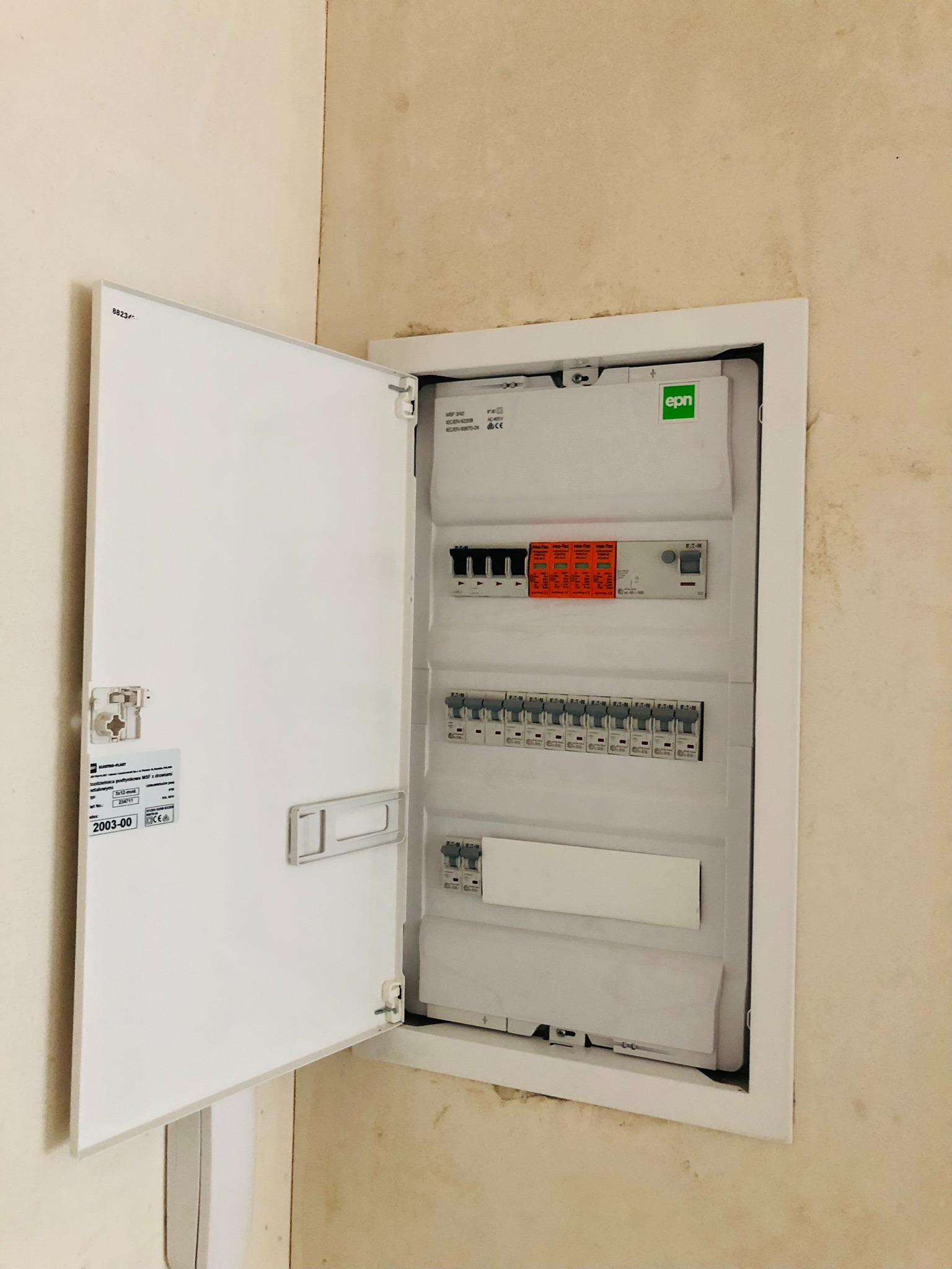 Otwarta skrzynka rozdzielcza z bezpiecznikami i wyłącznikami zamontowana na ścianie w surowym stanie.