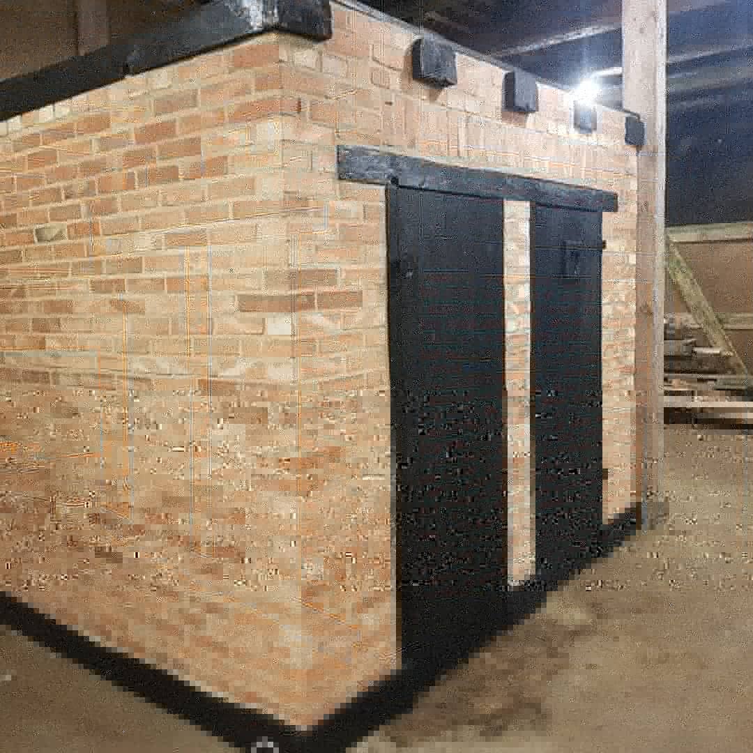 Murowana budowla z cegły z czarnymi, przesuwnymi drzwiami i elementami wykończeniowymi pod dachem, prawdopodobnie węzeł sanitarny w Swołowie, w trakcie budowy lub tuż po jej zakończeniu.