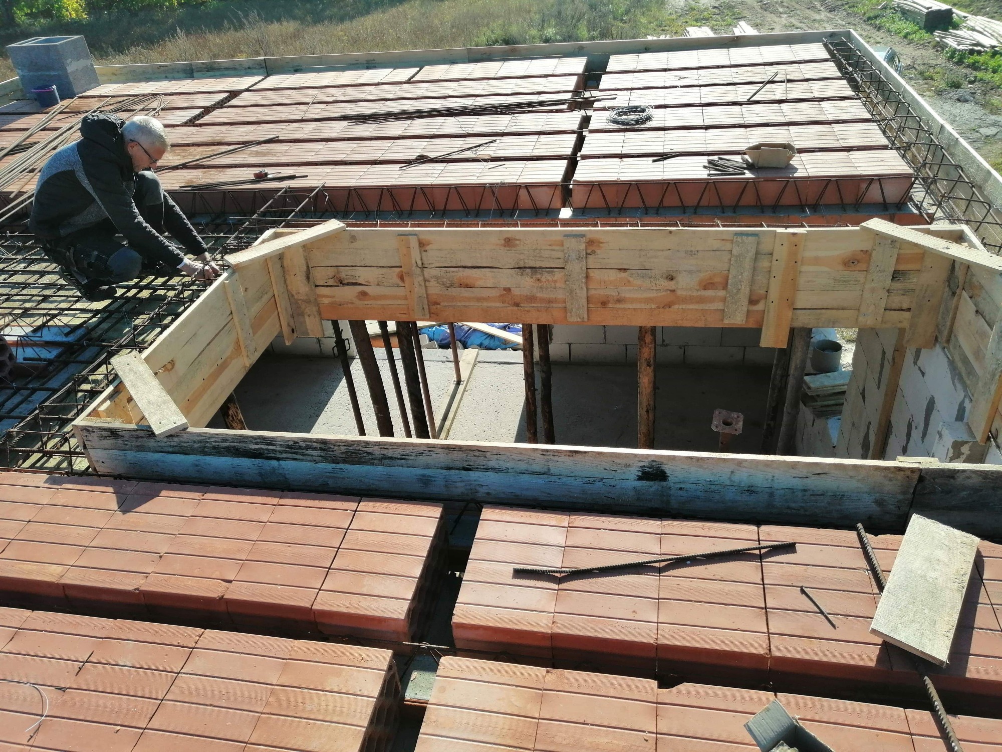 Pracownik w trakcie montażu zbrojenia i szalunku na stropie Teriva z pustaków ceramicznych, widok z góry na budowę domu.