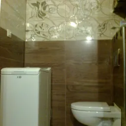 Ukończona łazienka z beżowo-brązowymi płytkami z motywem roślinnym, białą pralką i podwieszaną toaletą.