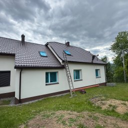 Promal-Dach - Dom jednorodzinny z brązowym dachem, zabezpieczonymi oknami i drabiną. Widoczny fragment elewacji po malowaniu. Pochmurne niebo w tle.