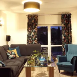 Salon z narożną sofą, turkusowym fotelem i ścianą z cegły, oświetlony lampą sufitową i wiszącą, z roślinami doniczkowymi i dekoracjami na szklanym stoliku kawowym.