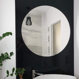 Jarońska Wnętrza projektowanie wnętrz - Nowoczesna łazienka z okrągłym lustrem w czarnej ramie, białą umywalką w kształcie łzy i widoczną w odbiciu ścianą z marmurowym wzorem oraz grzejnikiem drabinkowym