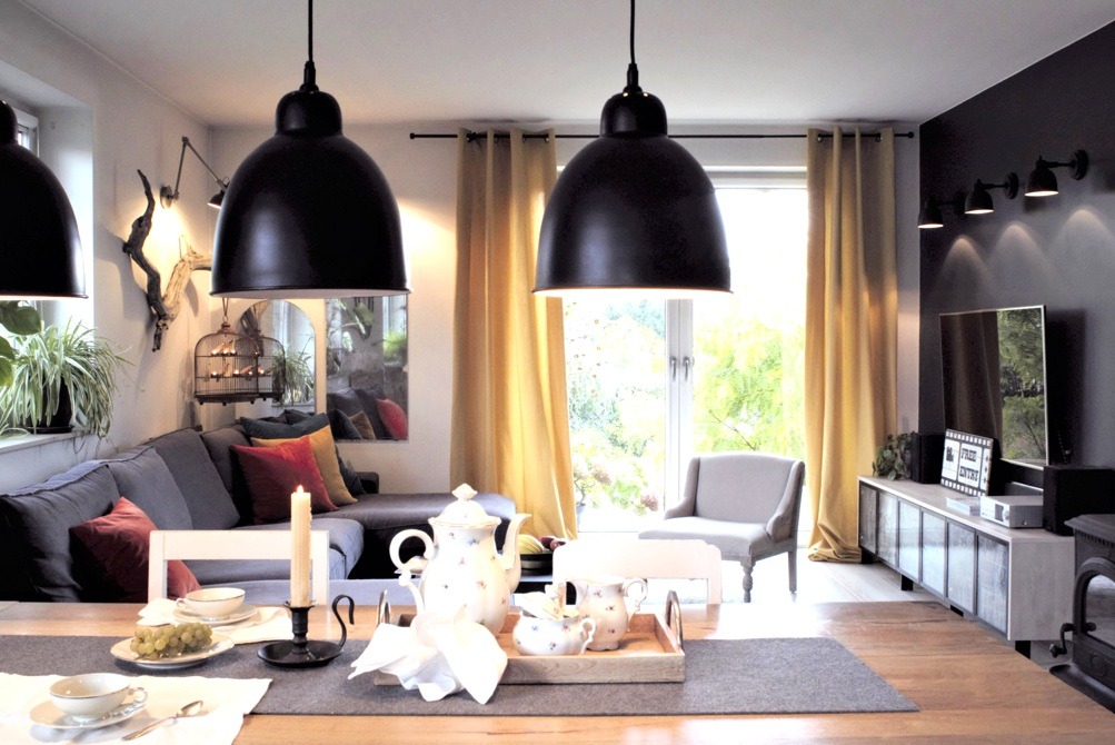 Salon z szarą sofą, czarnymi lampami wiszącymi i stołem z porcelanowym serwisem do herbaty, oświetlony światłem dziennym wpadającym przez okno.