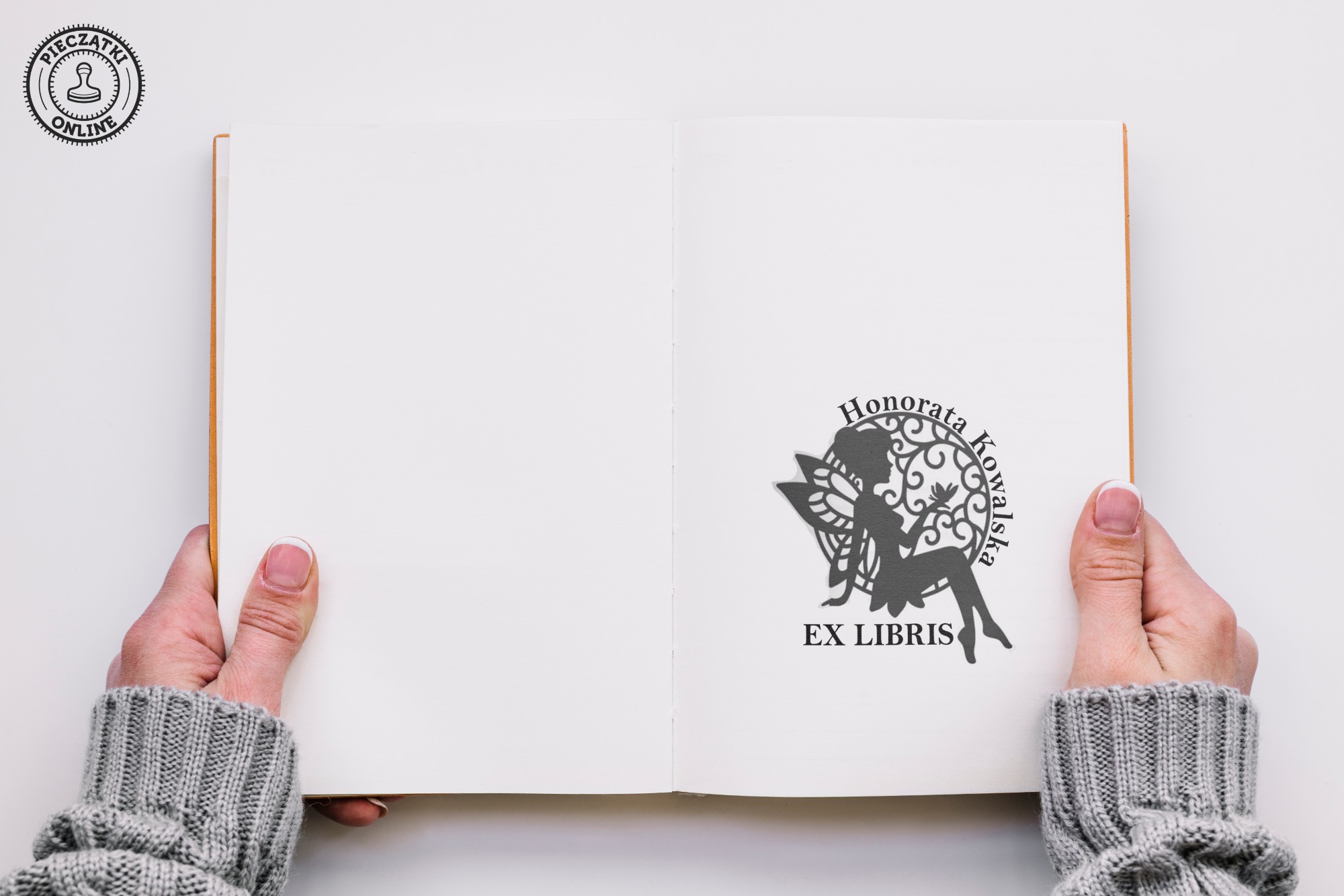 Otwarta książka z ekslibrisem w postaci sylwetki wróżki z imieniem i nazwiskiem Honorata Kowalska, trzymana przez osobę w szarym swetrze.