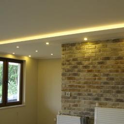 Remdom - Pokój z wykończoną ścianą z cegły dekoracyjnej, podwieszanym sufitem z oświetleniem punktowym i oknem z widokiem na zieleń.