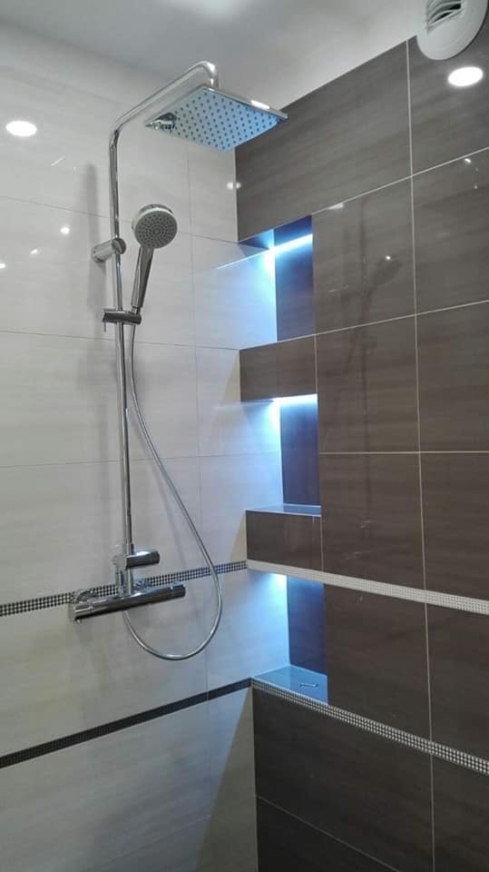 Nowoczesna łazienka z chromowaną armaturą prysznicową i wnękami z podświetleniem LED w szarych płytkach.