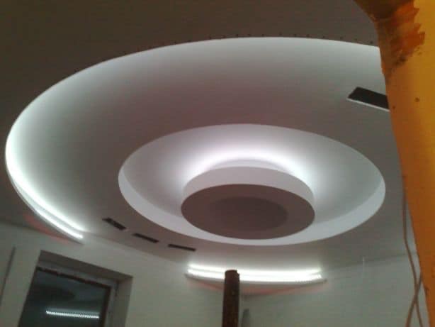 Nowoczesny sufit podwieszany z okrągłymi elementami i podświetleniem LED, widok z dołu.