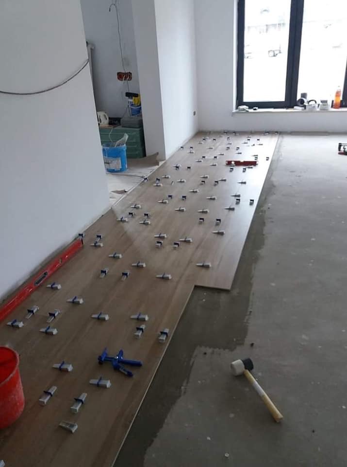 Układanie paneli podłogowych w jasnym odcieniu drewna, z użyciem niebieskich narzędzi do regulacji odstępów, widoczny gumowy młotek i poziomica.