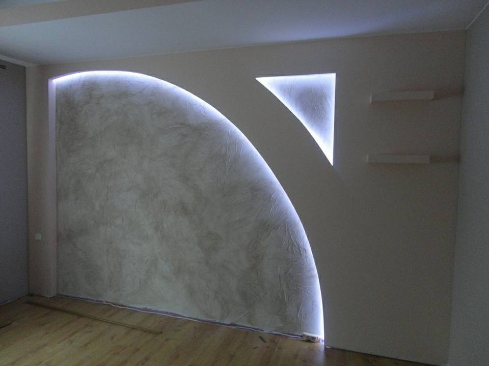 Dekoracyjna ściana z oświetleniem LED w kształcie łuku i trójkąta, wykończona gładzią strukturalną, widoczne drewniane panele podłogowe i minimalistyczne półki.