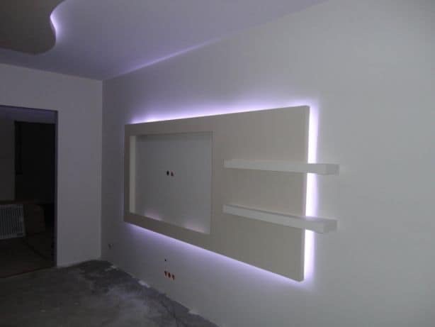 Biała ściana z podświetlanym panelem dekoracyjnym i półkami, w surowym stanie, z widocznymi kablami elektrycznymi, przed wykończeniem podłogi.