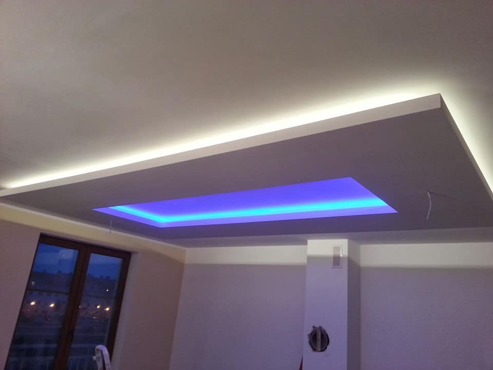 Nowoczesny sufit podwieszany z oświetleniem LED w kolorze niebieskim, widok z dołu, fragment okna w tle.