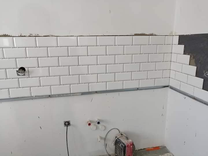 Białe, prostokątne płytki ułożone na ścianie w trakcie wykańczania łazienki, widoczne niedokończone krawędzie i przygotowane otwory na instalacje.