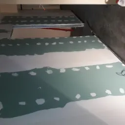 Ściana z zieloną płytą kartonowo-gipsową, częściowo wyszpachlowana, widoczne ślady po wkrętach i łączeniach, metalowy profil w tle, surowy stan wykończenia wnętrza.