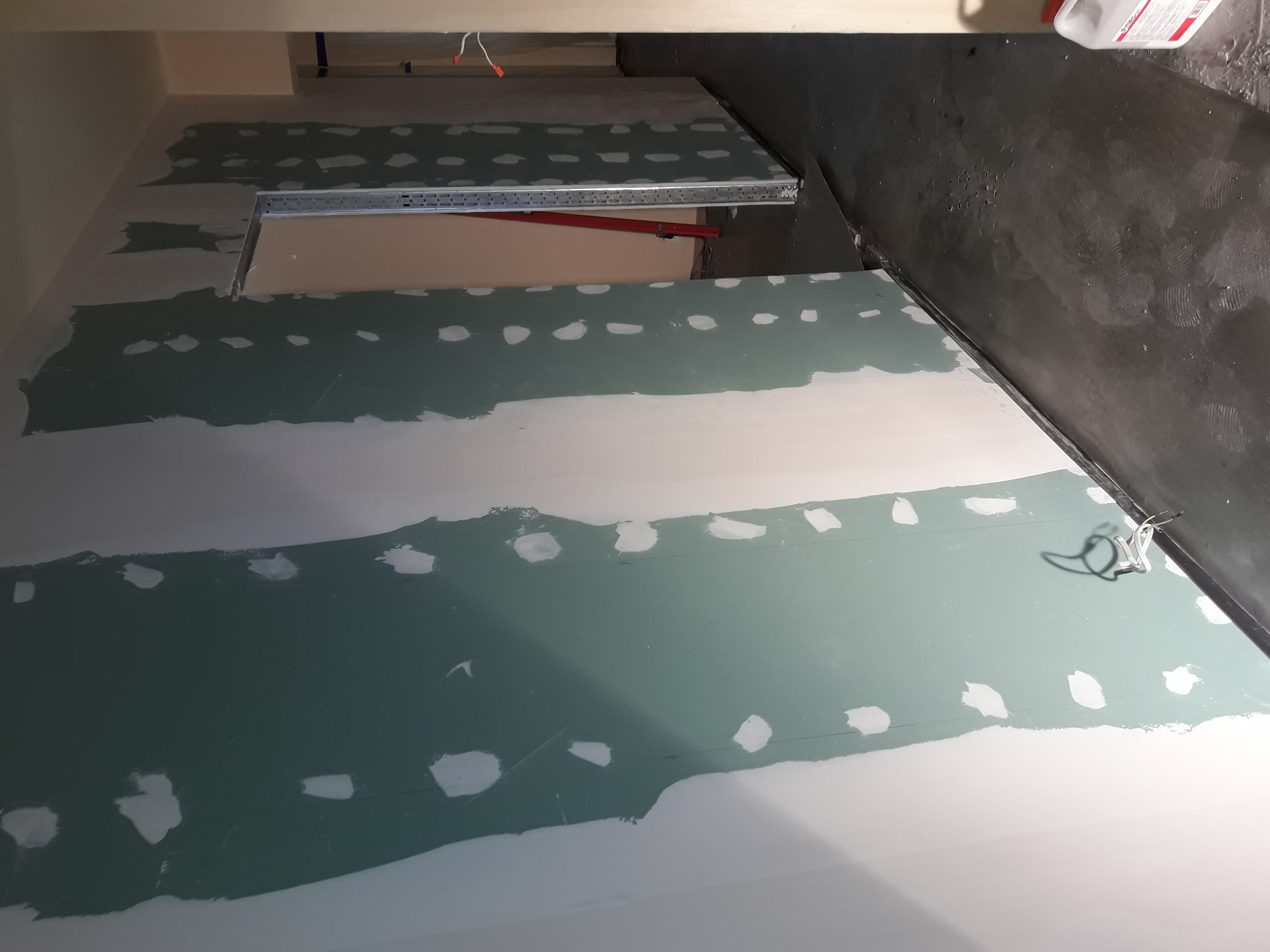 Ściana z zieloną płytą kartonowo-gipsową, częściowo wyszpachlowana, widoczne ślady po wkrętach i łączeniach, metalowy profil w tle, surowy stan wykończenia wnętrza.