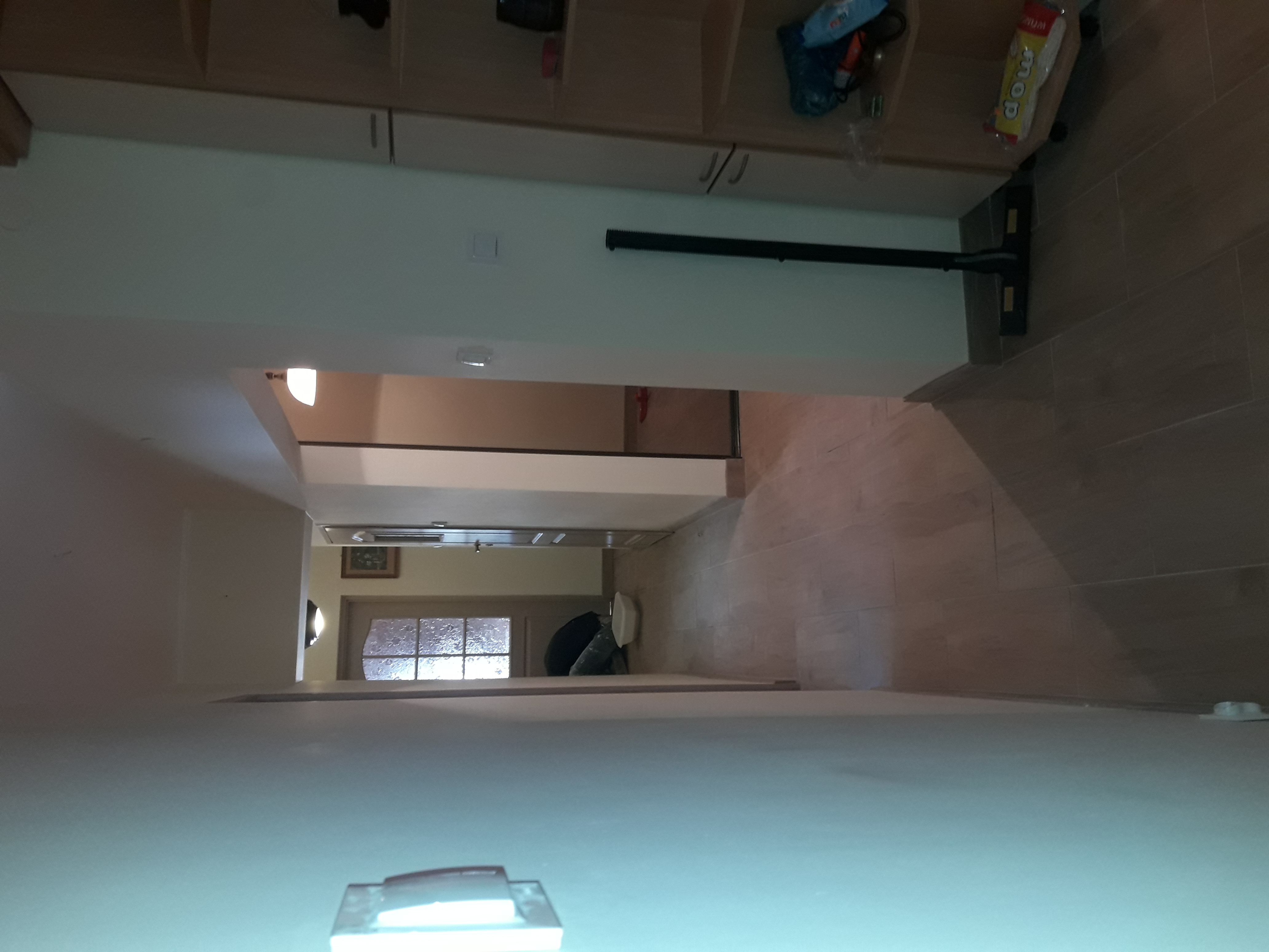 Długi korytarz z brązowymi płytkami podłogowymi i świeżo wygładzonymi ścianami, widok w perspektywie, z widocznym oświetleniem sufitowym i częściowo widocznym wyposażeniem.