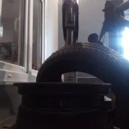 Opona na montażownicy w warsztacie, widok z dołu na tle okna.