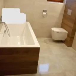 Nowoczesna łazienka z wanną obudowaną drewnem, beżowymi płytkami i podwieszaną toaletą.