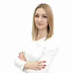 Portret kobiety z blond włosami w białym uniformie medycznym, z rękami skrzyżowanymi na piersi, na białym tle.