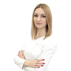 Portret kobiety z blond włosami w białym uniformie medycznym, z rękami skrzyżowanymi na piersi, na białym tle.