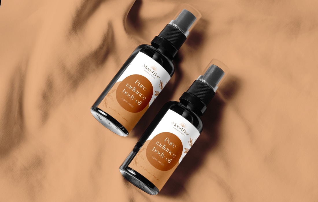 Dwa flakony czarnego olejku do ciała z minimalistyczną etykietą 'Mood Bar' na beżowym, lekko pofałdowanym tle.