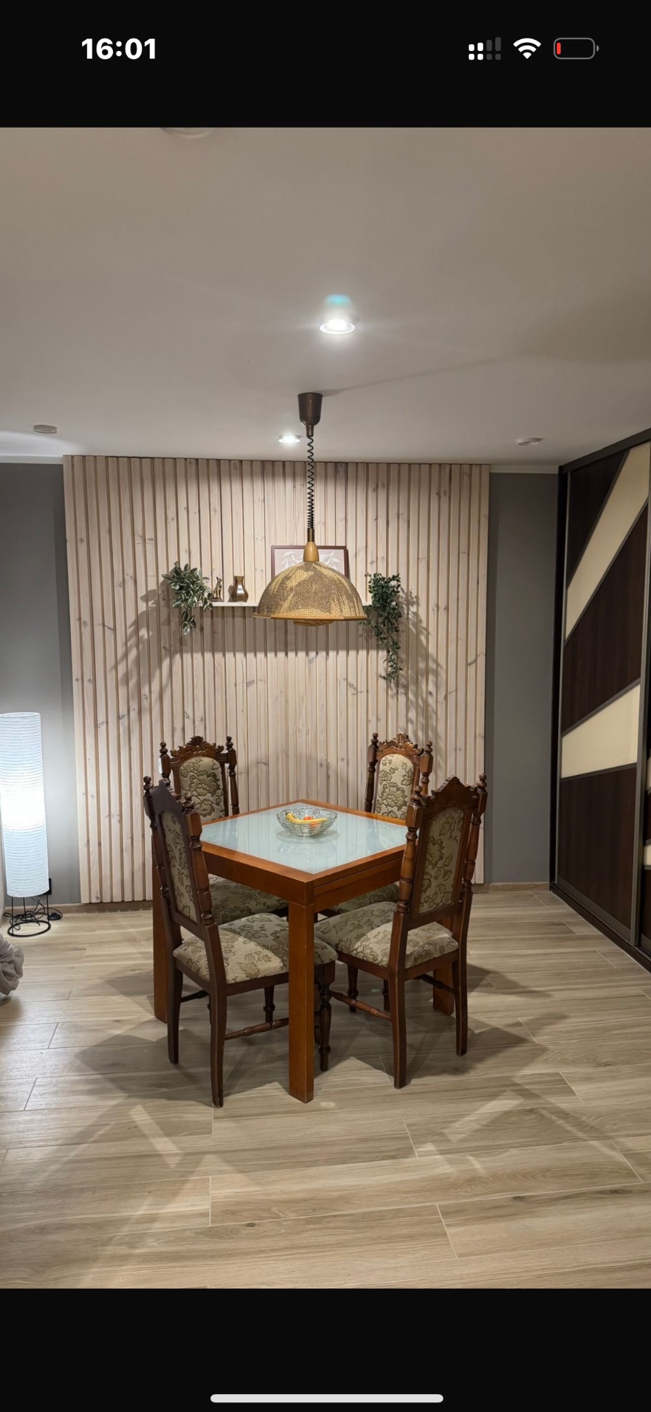 Jadalnia z drewnianym stołem i krzesłami w stylu vintage, podłoga wyłożona panelami imitującymi drewno, ściana z drewnianych paneli, lampa wisząca z abażurem.