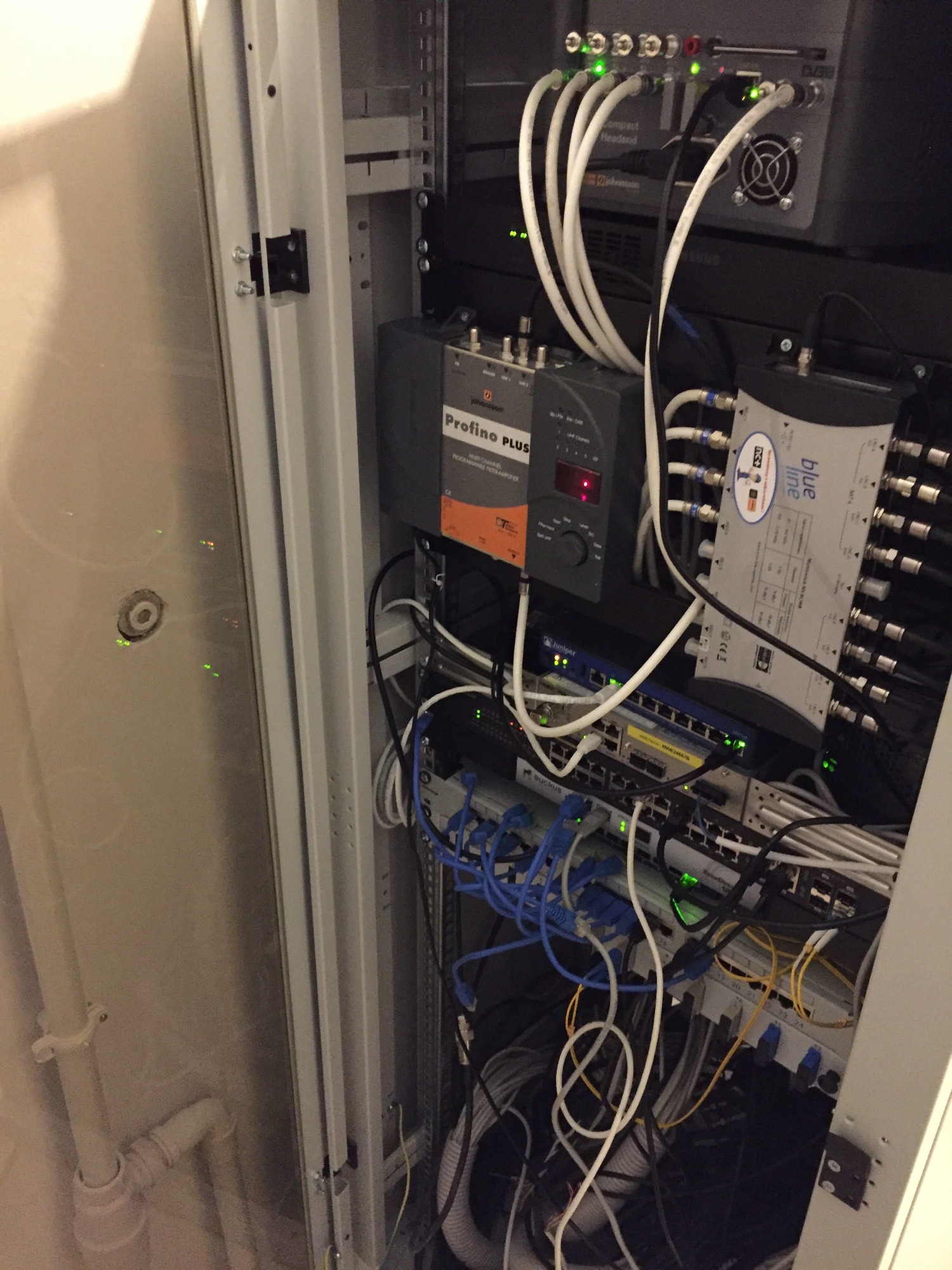 Widok z boku na otwartą szafę rack z zainstalowanymi urządzeniami sieciowymi, w tym routerami, przełącznikami i wzmacniaczami sygnału, z widocznymi kablami połączeniowymi.