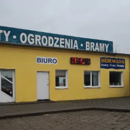 Żółty budynek firmy oferującej rolety, ogrodzenia i bramy, z wyświetlaczem temperatury pokazującym 3 stopnie Celsjusza, oraz widocznymi oknami i drzwiami.