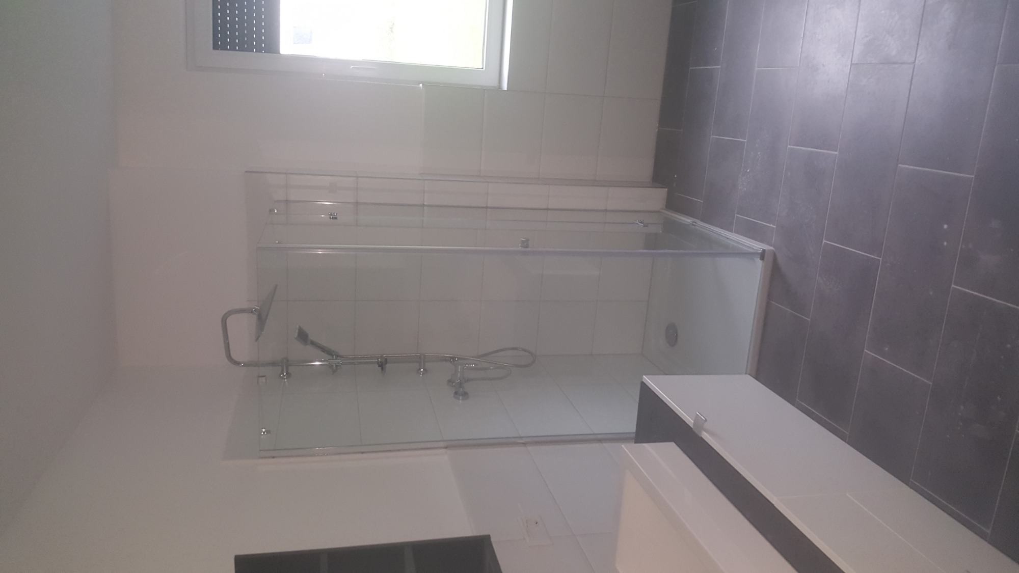 Nowoczesna kabina prysznicowa z chromowaną armaturą i białymi płytkami wewnątrz, na podłodze ciemnoszare płytki, widok z góry.