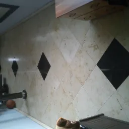 Beżowa podłoga z kwadratowych płytek kamiennych ułożonych w romby, z wstawkami z czarnych płytek, widoczny fragment drabinki gimnastycznej i piłka do koszykówki.