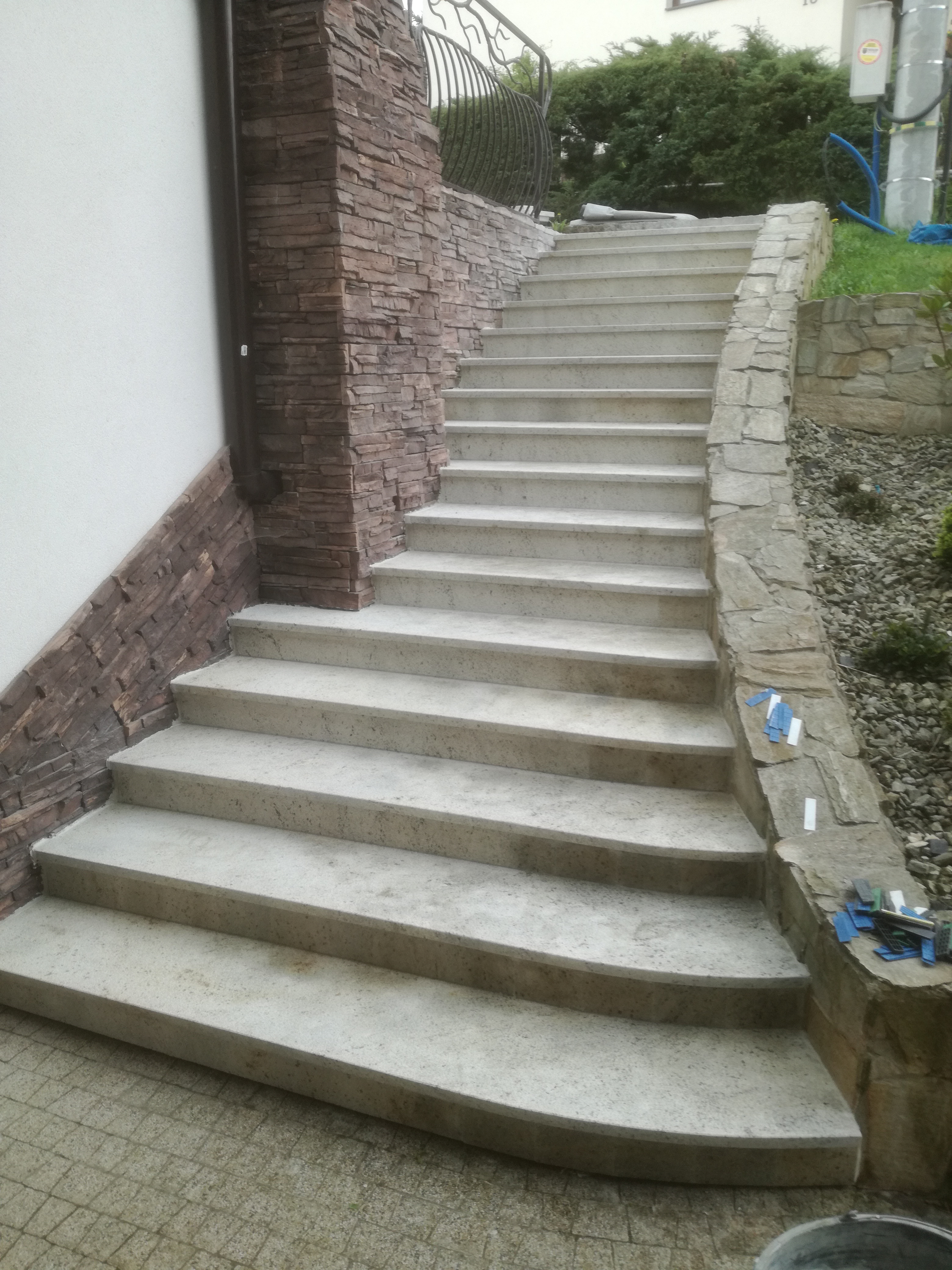 Betonowe schody zewnętrzne z kamienną obudową, prowadzące do ogrodu, widoczne narzędzia glazurnicze na krawędzi.