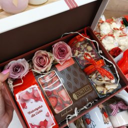 P.H.U. Termix A.J-BUD Jacek Ciekot - Otwarty, brązowo-biały karton prezentowy wypełniony czekoladą Cortez, słoikami z orzechami i suszonymi kwiatami, ozdobnymi różami oraz kubkiem z motywem buldoga francuskiego i napisem 'Love Me'.
