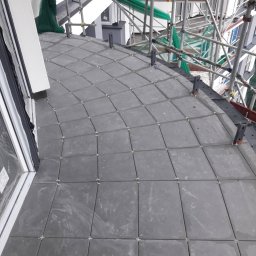 Jaroslaw Stefaniak - Szare płytki ułożone na balkonie, widoczne krzyżyki dystansowe, rusztowanie w tle.