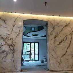 Jaroslaw Stefaniak - Ściana z efektem marmuru, oświetlenie LED przy suficie, widoczny fragment sufitu z dekoracyjnym wzorem Yin Yang, drabina oraz wiaderka farby w tle, pomieszczenie w trakcie prac wykończeniowych.