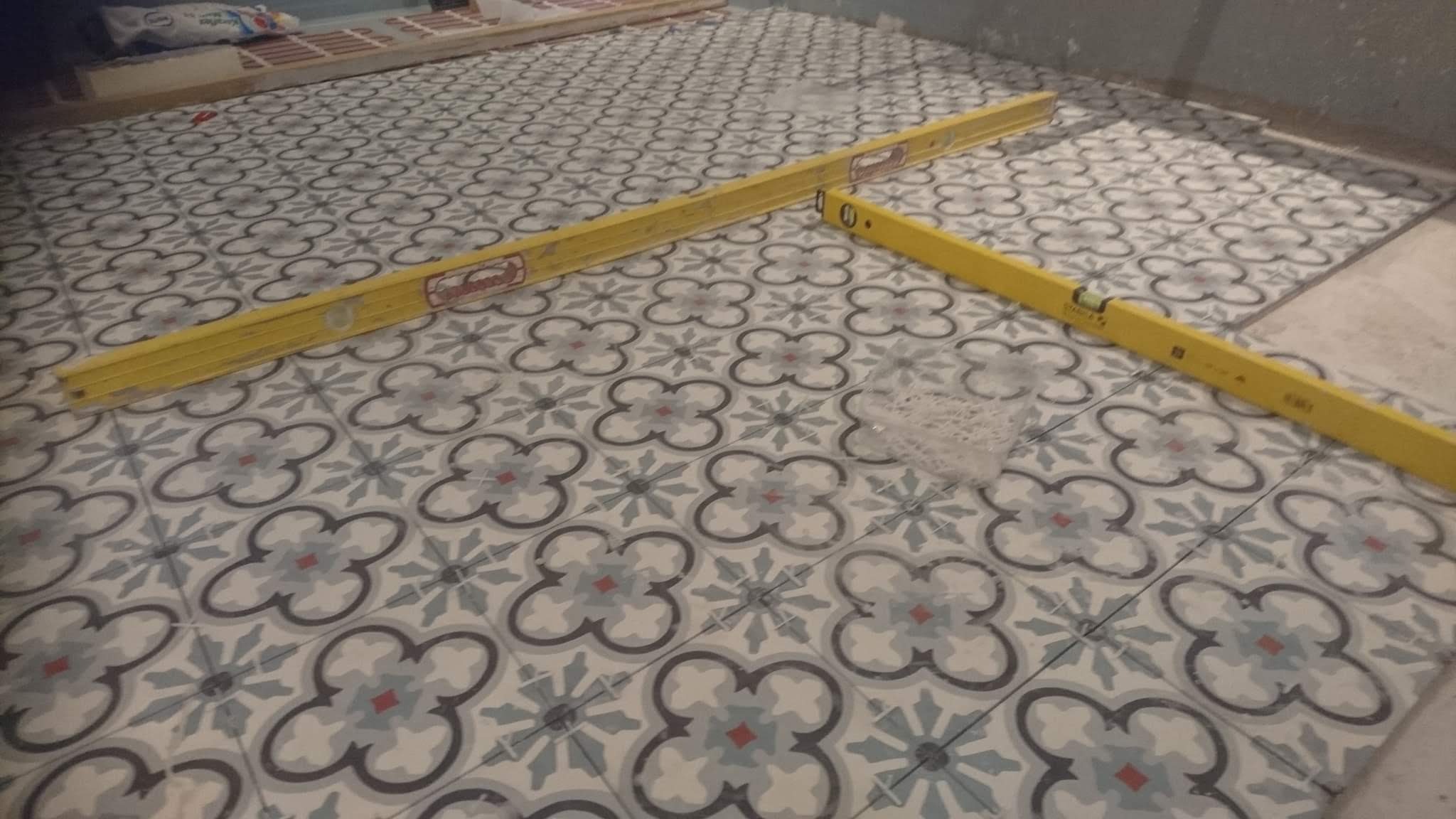 Ułożone płytki podłogowe z wzorem kwiatowym, sprawdzane poziomicą, widoczne pozostałości po opakowaniu fugi.