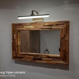 Hydro Fach Usługi Remontowo Budowlane - Łazienkowe lustro w ramie z nieregularnych kawałków drewna, oświetlone lampą LED, zawieszone na ścianie z białych płytek.