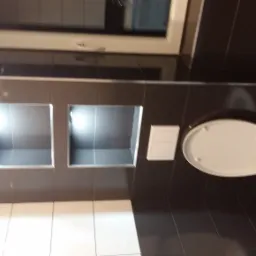 Nowoczesna łazienka z czarnymi płytkami, podświetlanymi niszami i podwieszaną toaletą z otwartą klapą.