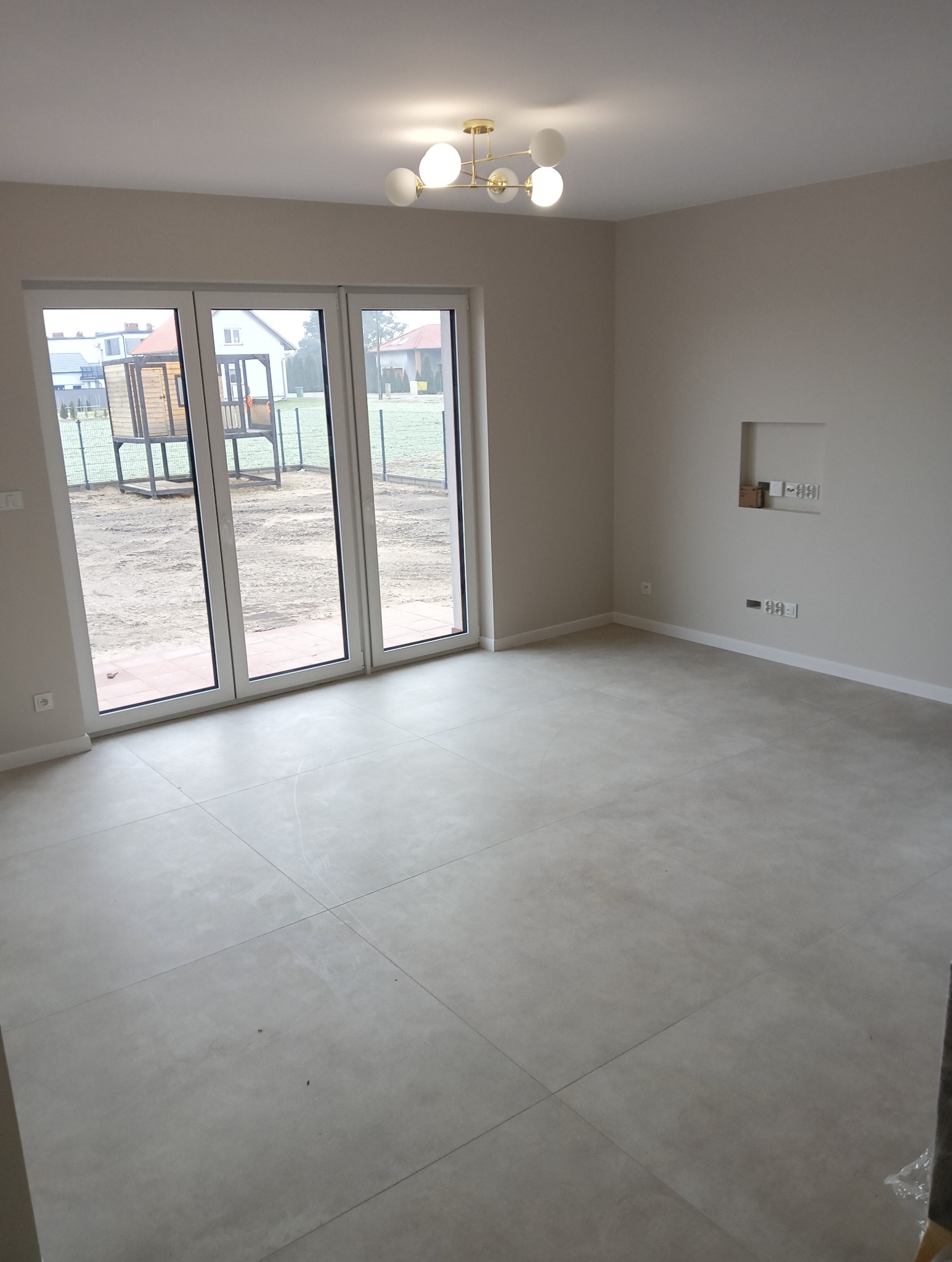 Jasne płytki podłogowe w pustym, nowym pokoju z dużym oknem balkonowym i nowoczesną lampą sufitową.