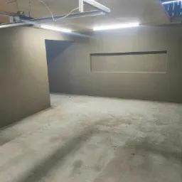 Wnętrze surowego pomieszczenia z świeżo nałożonymi tynkami, widoczna wnęka w ścianie i instalacja oświetleniowa pod sufitem z płyty OSB.