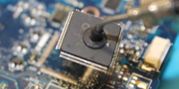 Lutowanie układu scalonego na płycie głównej laptopa, widoczne narzędzie lutownicze i komponenty elektroniczne w zbliżeniu.