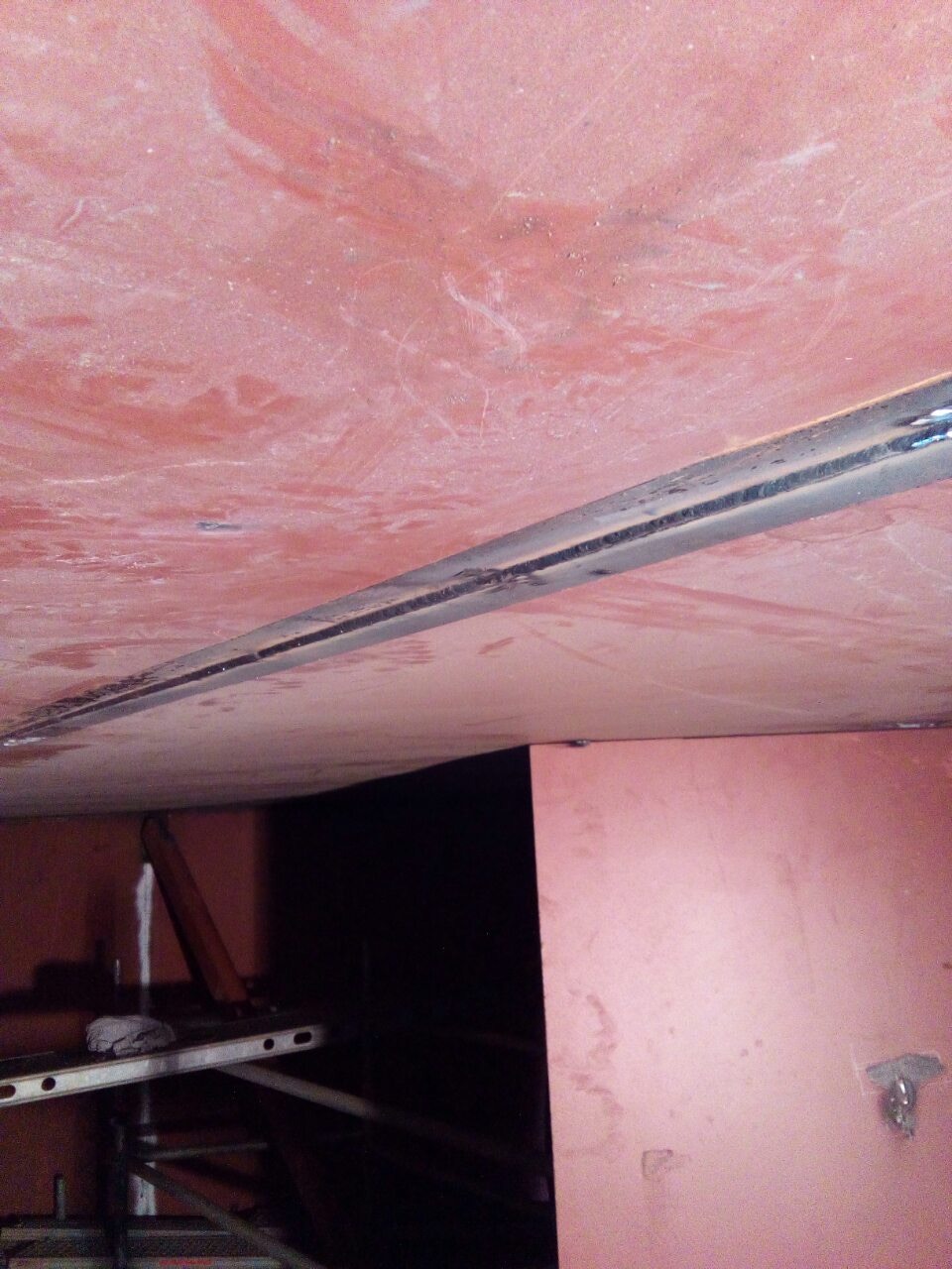 Wnętrze hali w trakcie budowy, widoczne stalowe elementy konstrukcyjne i fragment rusztowania, surowa powierzchnia ścian i stropu.