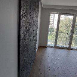 GOLD FINISH Filip Mróz - Ściana z dekoracyjną, ciemną strukturą w nowoczesnym wnętrzu z drewnianą podłogą i dużym oknem balkonowym.