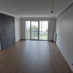 GOLD FINISH Filip Mróz - Pomalowane na szaro wnętrze mieszkania z panelami podłogowymi, ozdobną ścianą z efektem betonu i widocznymi puszkami elektrycznymi przed montażem osprzętu.