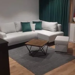 Nowoczesny salon z szarym dywanem, białym narożnikiem z zielonymi poduszkami i długimi, ciemnozielonymi zasłonami w tle.