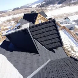 Dachy domów we Frydmanie pokryte ciemną blachą gontopodobną na tle zimowego krajobrazu górskiego, widok z góry.