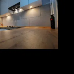 Fragment blatu drewnianego w kuchni z szarymi szafkami i oświetleniem LED, widoczny z niskiej perspektywy.