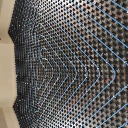 Niebieskie rury ogrzewania podłogowego ułożone na czarnej płycie montażowej z wypustkami, widok z góry, gotowe do zalania wylewką.