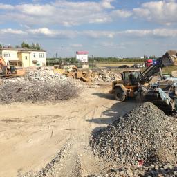 Usługi Transportowe, Wykopy, Rozbiórki, Handel - Prace rozbiórkowe z użyciem koparki i przesiewacza gruzu na placu budowy, widoczne zbrojenia i stosy gruzu.