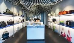 Wnętrze sklepu Bottletop z recyklingu, ściany drukowane w 3D, oświetlone półki z torebkami i plecakami, sufit z ażurową instalacją.